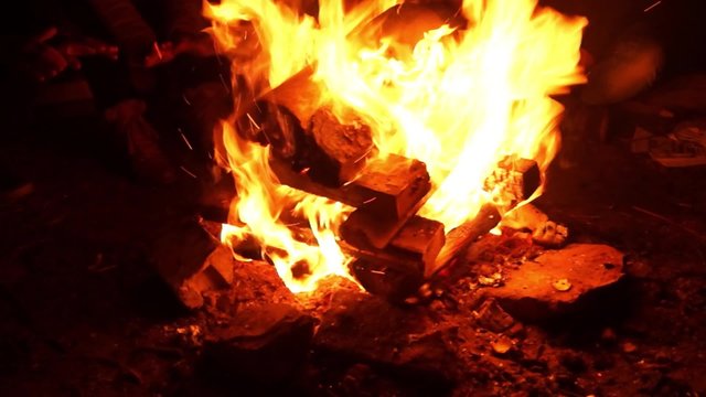 People warm hands around the campfire at night
