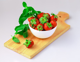 Macro strawberries close up in a white bowl on cutting board.