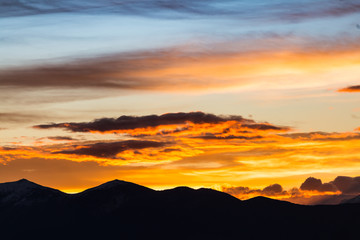 Fototapeta premium Majestic vivid sunset/sunrise with clouds over dark mountains silhouettes