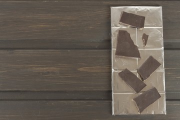 Chocolate wrapped in aluminum foil on a dark wooden board. Wrapped sweet treat.
