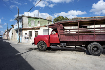 Kuba, Camagüey: Alter roter LKW parkt auf der Strasse der kubanischen Kleinstadt mit kleinen Häusern und blauem Himmel im Hintergrund