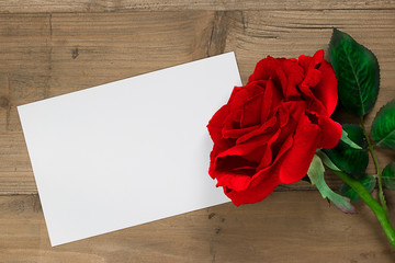 Red rose with blank paper.
Wooden background.