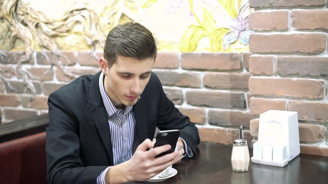 Business man drinking a cup of coffee while sitting with his phone in cafe.