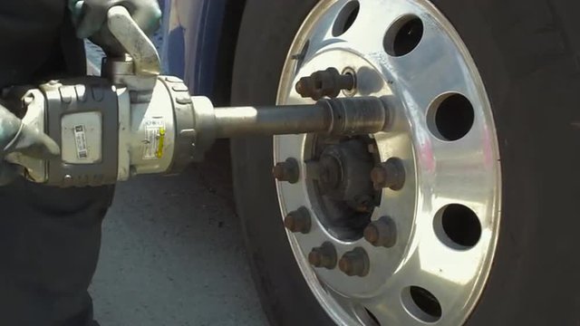 Auto mechanic removing nuts from convex freight liner truck tire