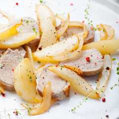 Pork tenderloin roasted with pear and onion on a white plate
