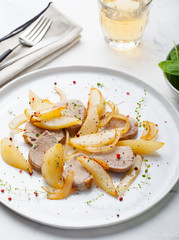 Pork tenderloin roasted with pear and onion on a white plate