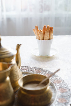 Shortbread biscuits in white cup and woman stirring tea in a cup in the background. Biscuits are the food specialty of Lanquedoc region of France, called zezette. Selective focus.