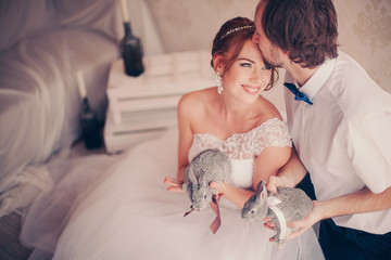 beautiful smiling bride with rabbits in her hands kissed by the groom in warm colors 