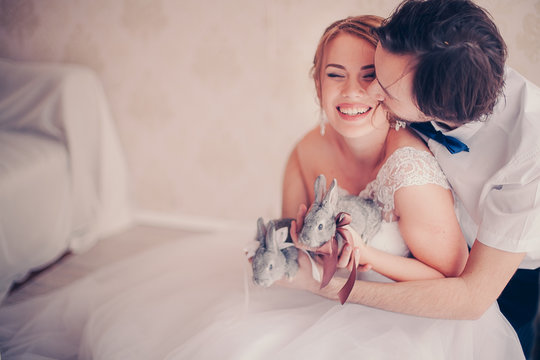 closeup photo ofbeautiful smiling bride with rabbits in her hands kissed by the groom in warm colors 