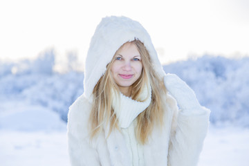 Beautiful smiling woman wearing a fur coat and hood over snow in winter day