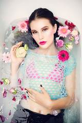 Fototapeta premium Portrait of beautiful young brunette girl with bright makeup lying in the bath with flowers, the concept of health and beauty