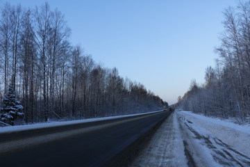 Трасса со снегом по обочинам и в окружении деревьев зимним ранним утром