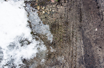 Tire tracks on the sand. Wheel tracks on dirt. Dark tire tracks background with snow and water. Wheel track on muddy ground. The trace of a tyre in the sand