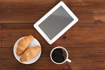 Coffee digital tablet and croissants on a wooden table.