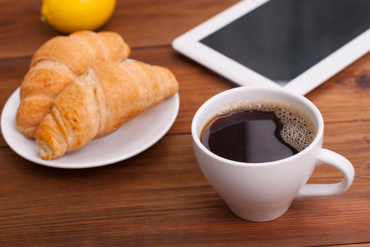 Cup of coffee and a croissant on the table tablet.