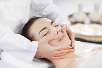 Fototapeta na wymiar Beautiful young woman relaxing with face massage at beauty spa