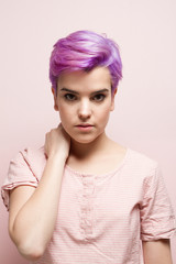 Violet-short-haired woman in pink pastel holding her nape, indoo
