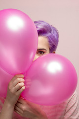 Violet short-haired woman in pink pastel peeking behind balloons
