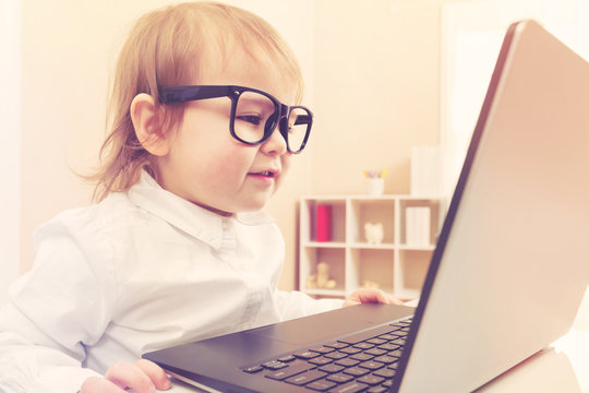 Smart toddler girl wearing big glasses using her laptop