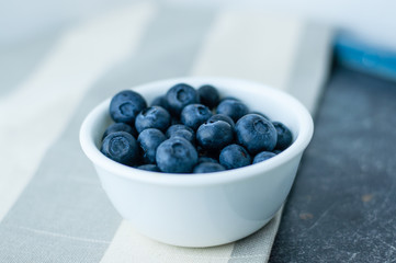 Small white bowl of blueberries linen tablecloth close up, side view