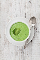 Spinach cream soup in bowl on white rustic table, top view