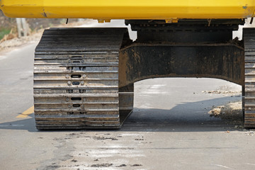 center of left caterpillar wheel (selected focus) of yellow track-type loader excavator with shadow on road in construction site