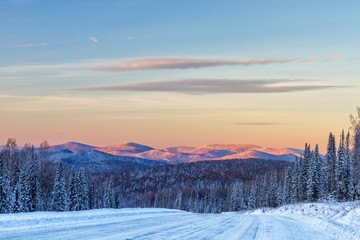 Winter road in mountains ,forest and mountain peaks in background at sunrise in Sheregesh, Siberia