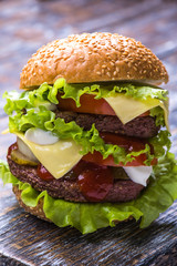 Hamburger with beef cutlet, fresh vegetables: tomatoes, onions, lettuce, sauce and bun with sesame seeds on a wooden background