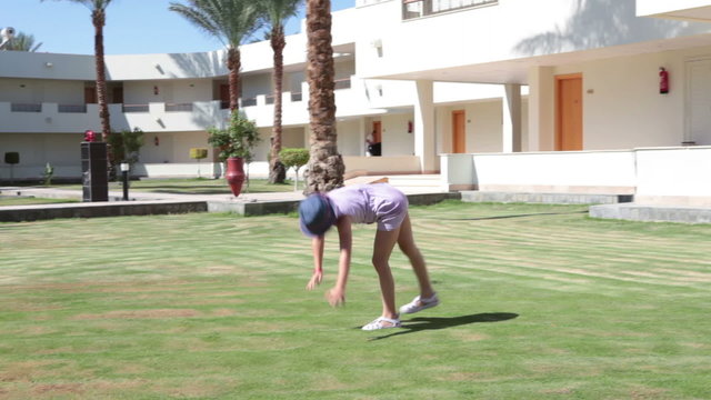 Young playful girl doing a circular sideways handspring with the arms and legs extended then cross split on the green lawn
