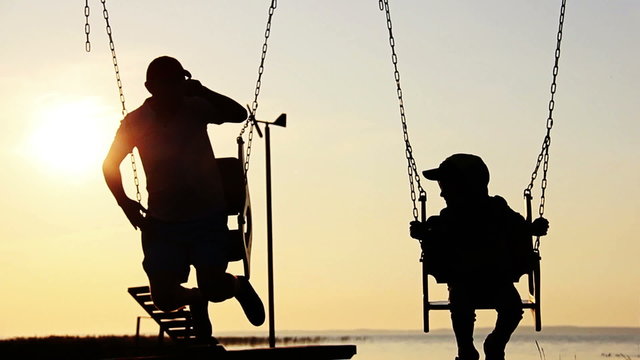 son and father swinging on a swing at sunset, dawn, near the river, silhouettes