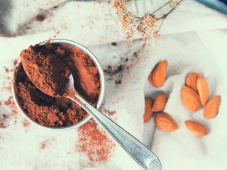 Cocoa powder in a glass on kitchen napkin with almonds and dried flowers, toned