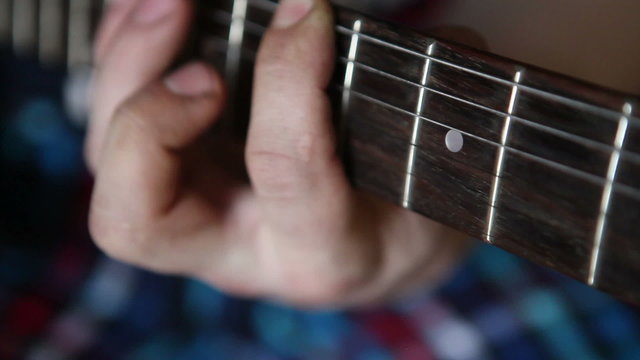 man plays guitar, his fingers on the fretboard closeup