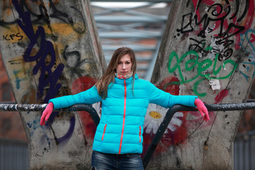 Obraz premium Beautiful blonde woman wearing jacket and pink gloves standing in front of graffiti