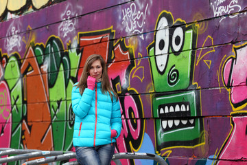 Beautiful blonde woman in jacket and blue jeans in front of a wall with graffiti