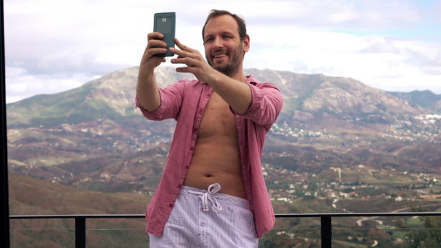 Man taking selfie photo with cellphone, on terrace with mountains view 4K
