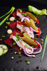herring appetizer with beets and gherkin on black slate board