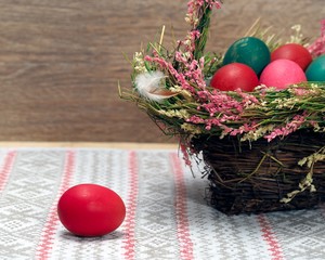Basket with Easter eggs. Eggs for Easter - red, green and pink in a basket decorated with flowers. Background - the wooden board