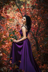 Fototapeta na wymiar Lady in a luxury lush purple dress ,fantastic shot,fairytale princess in walking in the autumn forest,fashionable toning,creative computer colors
