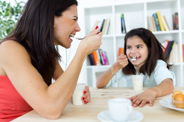 Beautiful mother and her daughter eating iogurt at home.