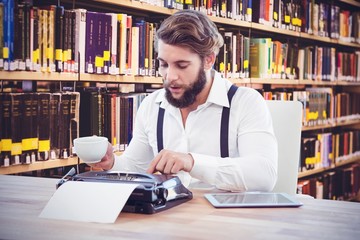 Fototapeta premium Composite image of hipster holding coffee working on typewriter
