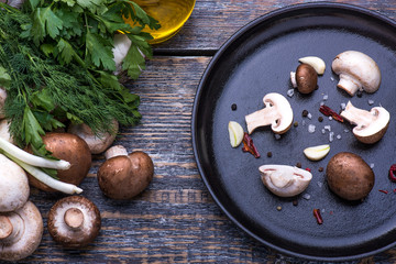 Mushrooms, parsley, dill, onion, olive oil, spices - ingredients for the preparation of mushroom dishes in a frying pan on a wooden background