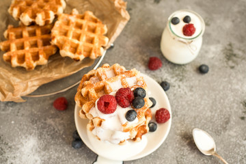 Homemade Belgian waffles with forest fruits, blueberries, raspberries over grey background. Vintage styling. Top view.
