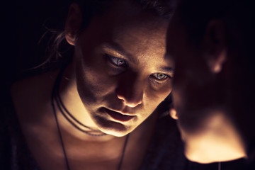 Dark portrait of mysterious sad looking woman looking at her own reflection