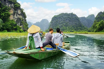 Rolgordijnen Tourists in boat. Rower using her feet to propel oars, Vietnam © efired