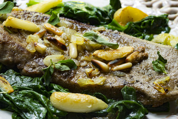 Gebratene Kalbsleber auf italienische Art mit Pinienkernen, Kräutern und Blattspinat als closeup