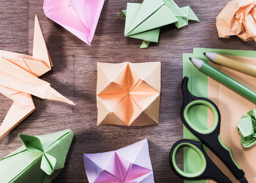 Origami figures, scissors and pencils on wooden table - flat lay, high angle.