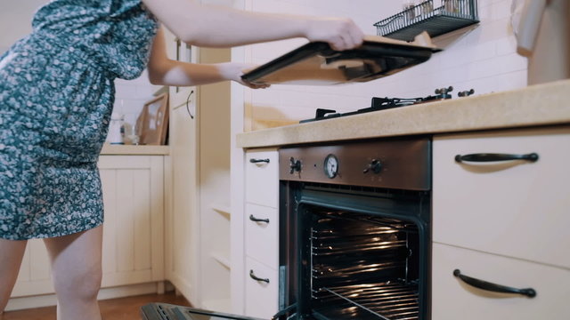Young woman put a pastry into an oven in the kitchen	