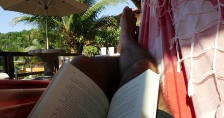 Man reading a book on the hammock in a summer day