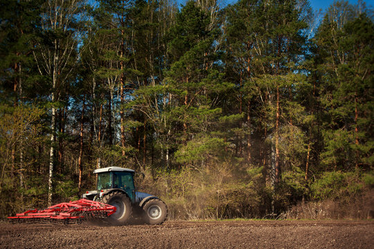 tractor with weeding-machine on edge of ploughed field at forest