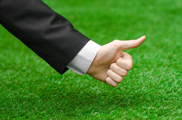 Nature and business topic: the hand of man in a black suit showing a thumbs up gesture against a background of green grass